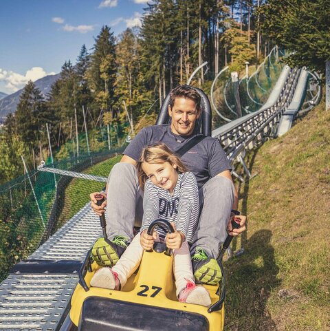 Arena Coaster Ein Mann und ein Mädchen fahren mit einer Sommerrodelbahn.
