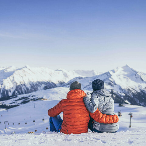 Gästezeitung Wald-Königsleiten Ein Mann und eine Frau sitzen im Schnee und blicken auf eine traumhafte Bergkulisse
