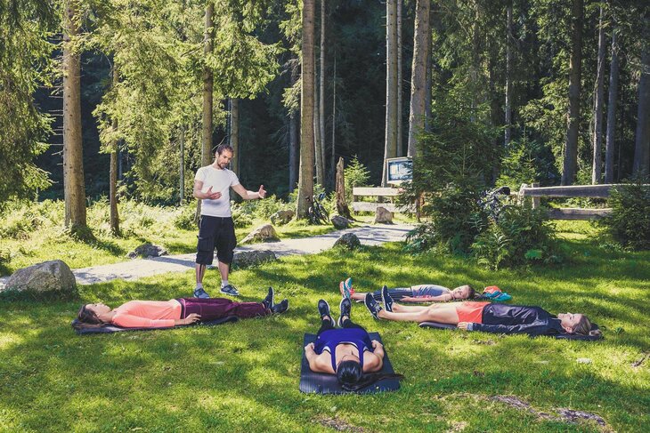 Vier Frauen liegen auf Matten in der Wiese, während ein Mann ihnen die Entspannungstechniken erklärt