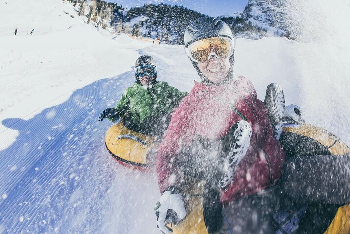 Zwei Personen fahren auf luftgefüllten Reifen die Piste hinunter