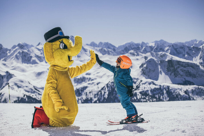 Ein kleiner Schifahrer gibt dem Maskottchen Funty ein High-Five