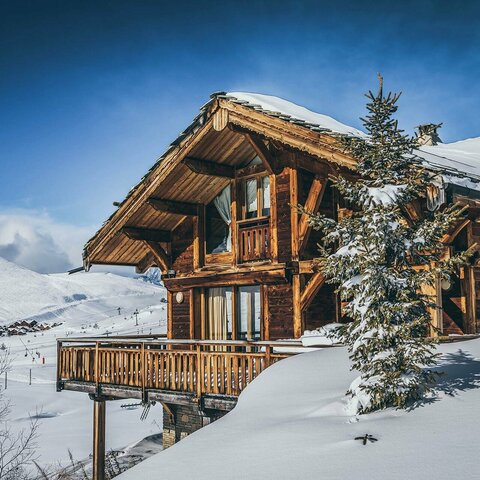 Unterkunftsanfrage Holzhaus, das von Schnee bedeckt ist, mit winterlicher Atmosphäre und verschneiten Bäumen rundherum
