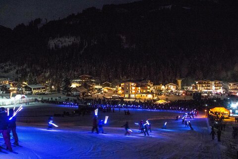 Viele Menschen beim Nachtschifahren, mit leuchtenden Skistöcken