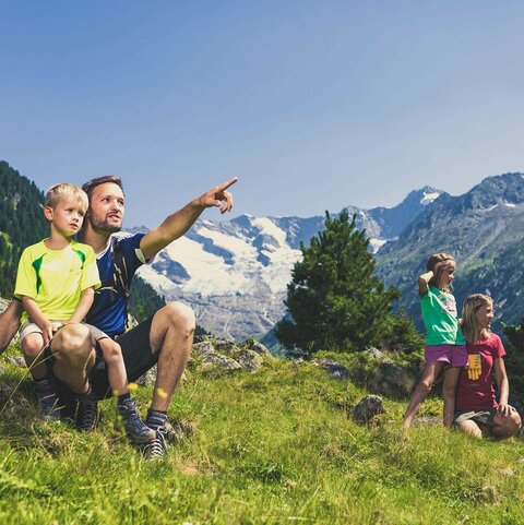 Eine Familie sitzt auf einer Wiese und blickt auf eine traumhafte Bergkulisse