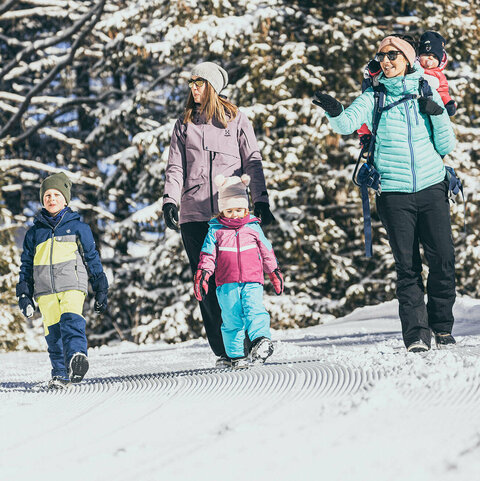 Zwei Frauen und drei Kinder spazieren durch den Schnee