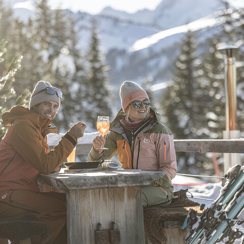 Ein Mann isst einen Kaiserschmarrn und eine Frau trinkt einen Aperol auf einer Hütte