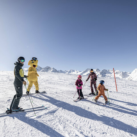Skischule & Skiverleih Eine Familie auf Skiern steht mit dem Maskottchen Funty auf der Piste