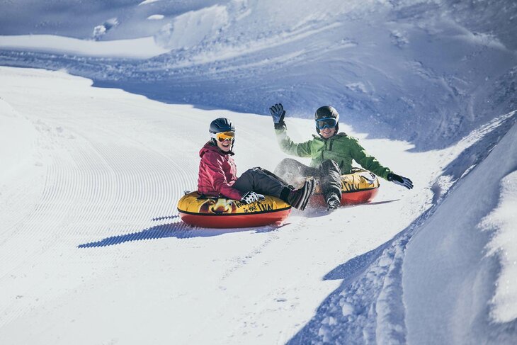 Zwei Personen fahren auf luftgefüllten Reifen die Piste hinunter