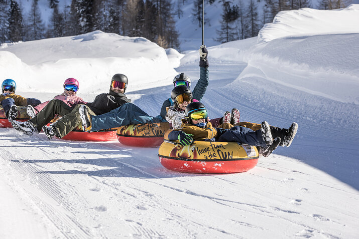 Eine Familie fährt auf Reifen die Piste hinunter