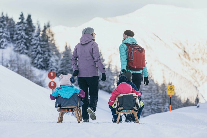 Zwei Frauen ziehen ihre Kinder durch den Schnee auf Rodeln