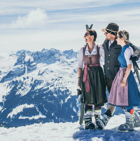Ein Mann und zwei Frauen in Trachtenkleidung stehen vor einer Traumhaften Bergkulisse