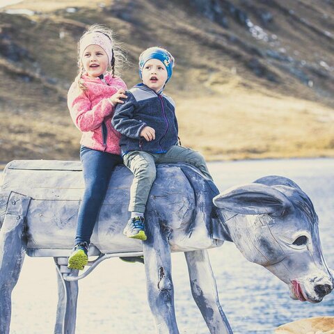 Zwei Kinder sitzen auf einer hölzernen Kuhstatue
