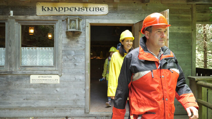 Ein Mann und zwei Frauen in Bergmannsuniform, verlassen die Knappenstube
