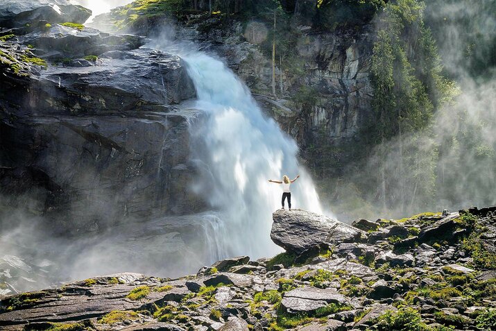 Eine Frau steht auf einem Stein vor einem großen Wasserfall