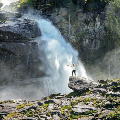Eine Frau steht auf einem Stein vor einem großen Wasserfall