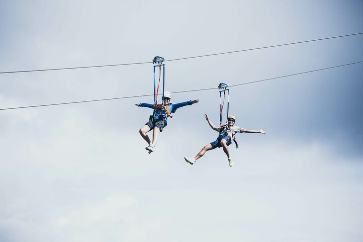 Zwei Personen fahren mit einer Zipline über der traumhaften Natur