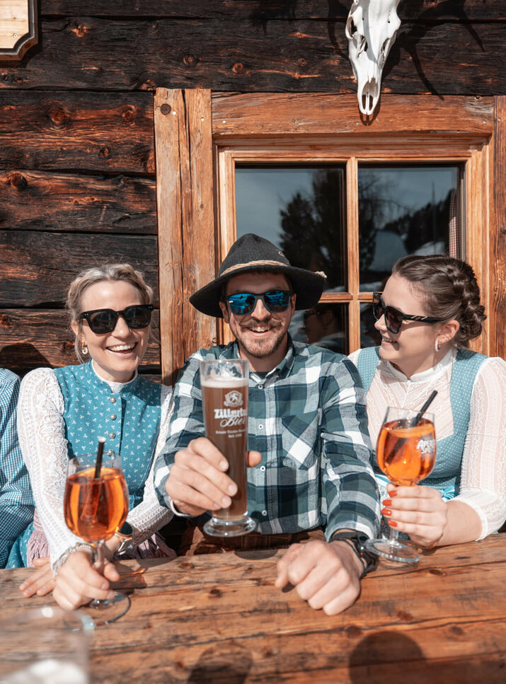 Zwei Frauen trinken einen Aperol und ein Mann trinkt ein Bier auf einer Hütte