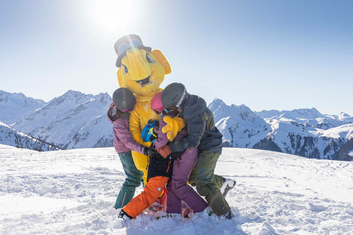 Eine Familie umarmt das Maskottchen Funty