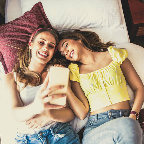 Zwei Frauen liegen auf einem Bett und machen ein Selfie