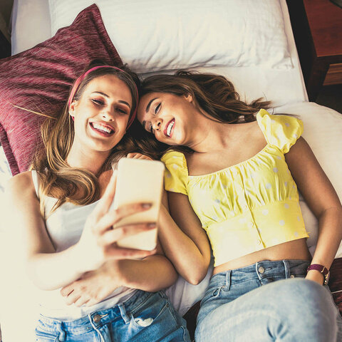 Zwei Frauen liegen auf einem Bett und machen ein Selfie