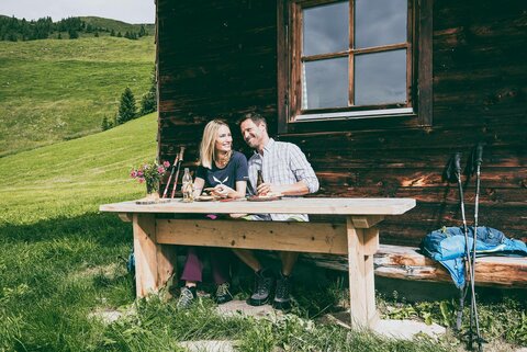 Ein Mann und eine Frau essen eine Brotjause bei einer Hütte