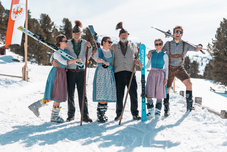 Drei Männer und drei Frauen in Trachtenkleidung mit Ski in der Hand im Schnee