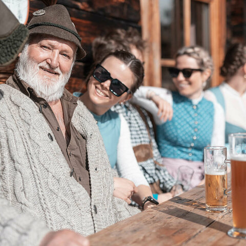Dirndl & Lederhosentage Männer und Frauen in Trachtenkleidung sitzen bei einer Hütte