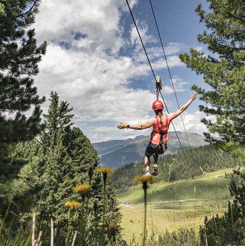Eine Frau rutscht auf einer Seilrutsche durch eine grüne Landschaft.