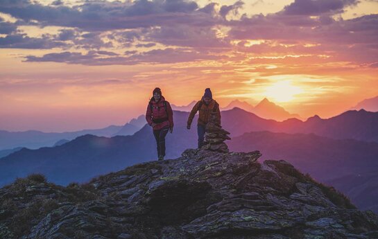 Ein Mann und eine Frau wandern am Kreuzjoch, mit traumhaften Sonnenaufgang im Hintergrund