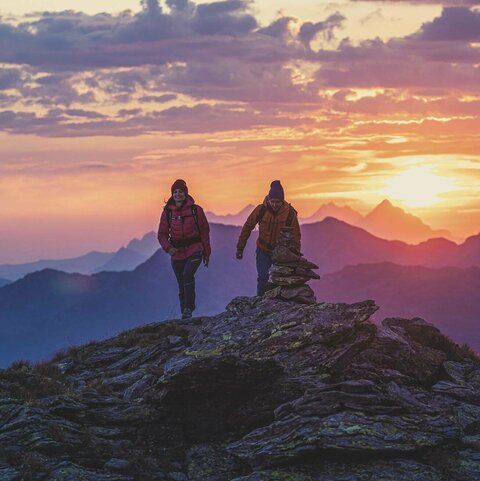 Ein Mann und eine Frau wandern am Kreuzjoch, mit traumhaften Sonnenaufgang im Hintergrund
