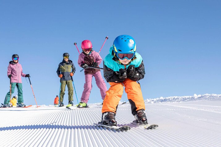 Eine Frau, ein Mann und zwei Kinder fahren die Piste hinunter