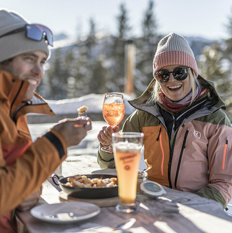 Mein Hüttengenuss Ein Mann isst einen Kaiserschmarrn und eine Frau trinkt einen Aperol auf einer Hütte