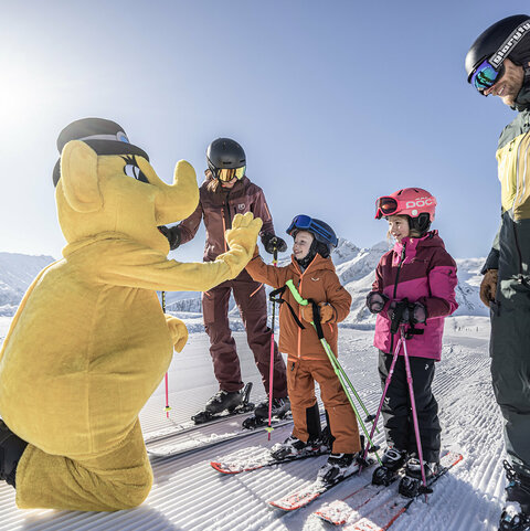Eine Familie auf Skiern mit dem Maskottchen Funty