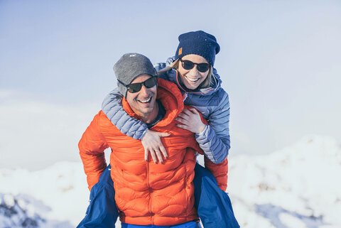 Ein Mann trägt eine Frau huckepack durch den frischen Schnee