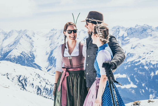 Ein Mann und zwei Frauen in Trachtenkleidung stehen vor einer Traumhaften Bergkulisse