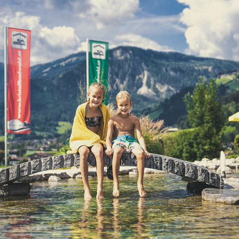 Ein kleiner Junge und ein Mädchen sitzen am Teich vor dem Kristallbad