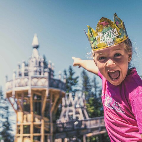 Ein Mädchen trägt eine Papierkrone und zeigt auf das Fichtenschloss.