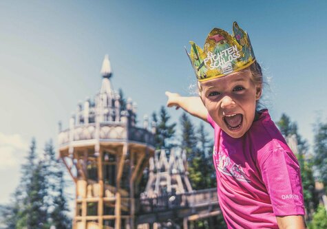 Ein Mädchen trägt eine Papierkrone und zeigt auf das Fichtenschloss.
