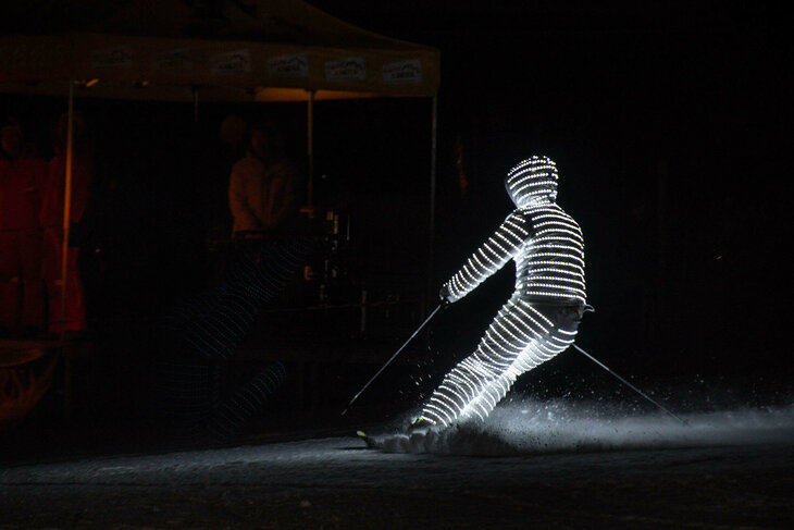 Ein Skifahrer ist von Kopf bis Fuß beleuchtet und fährt im Dunkeln die Piste herunter