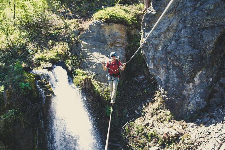 Ein Mann, in einem roten T-Shirt, klettert im Klettersteig Talbach