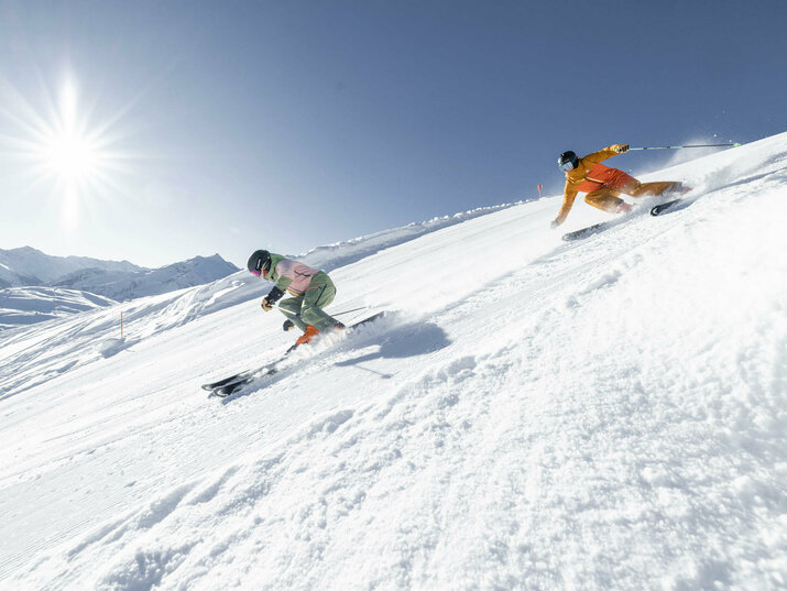 Zwei Skifahrer rasen die Piste hinunter