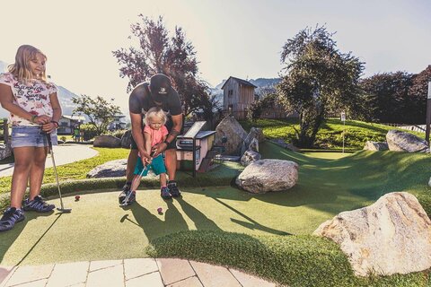 Ein Mann hilft einem kleinen Mädchen beim Minigolf spielen