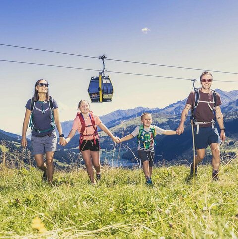 Openingstijden Kabelbanen Eine Familie spaziert händchenhaltend durch eine Wiese
