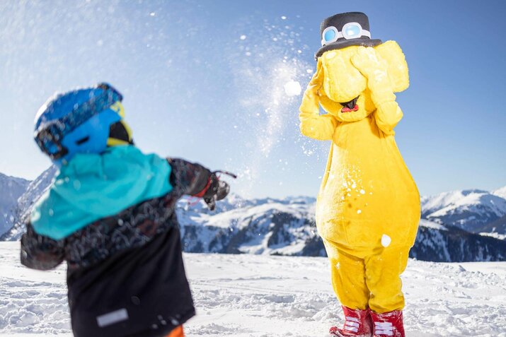 Ein Kind wirft Schneebälle auf das Maskottchen Funty