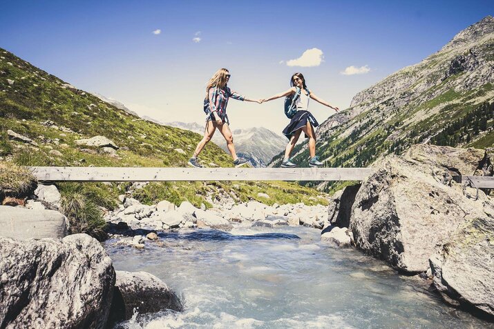 Zwei Frauen gehen händchenhaltend über eine Holzbrücke
